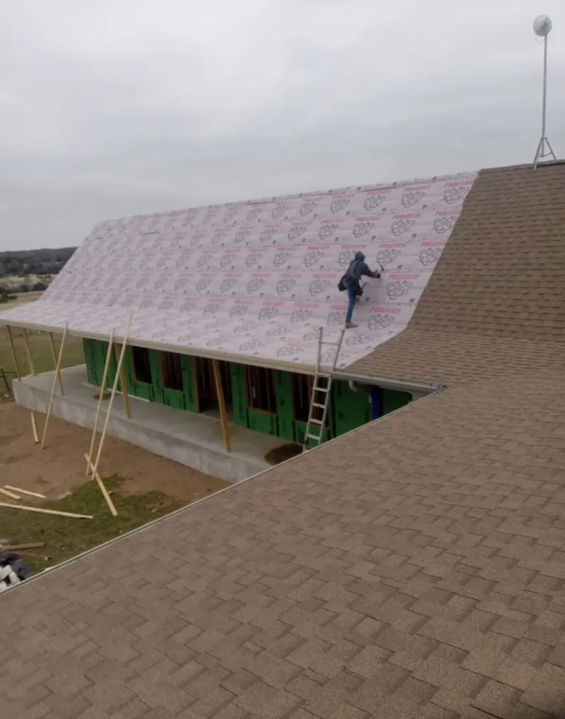 Worker preparing underlayment for a metal roof installation in Center